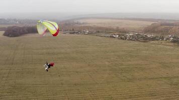 Mann mit ein Mantel fliegend auf ein Gleitschirm mögen ein Übermensch Über ein Gelb Herbst Feld. Aktion. fliegend Fallschirmspringer in der Nähe von das Dorf auf ein nebelig Tag. video