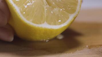 Squeezing lemon juice from a lemon half. Action. Close up of female hand getting lemon juice on a wooden board surface. video