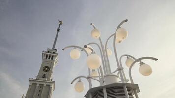 bas vue de une l'horloge la tour détails et une rue lampe tourné de pendant lumière du jour. action. magnifique la tour avec une flèche et une rue lumière sur bleu nuageux ciel Contexte. video