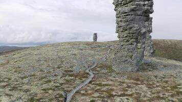 rots formaties Aan de top van een berg. klem. antenne visie van een toerist staand en op zoek Bij een reusachtig steen pijlers met bewolkt lucht en bebost heuvels Aan de achtergrond. video