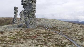 Natural stone sculptures on a hill top on cloudy sky background. Clip. A man looking very small near giant stone pillars, Manpupuner, Comi republic, Russia. video