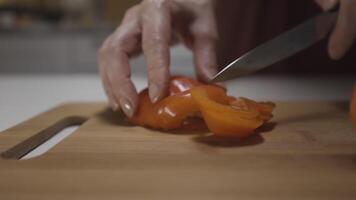 Female hands with a steel knife cutting pepper for salad, concept of healthy vegetarian food. Action. Close up of fresh pepper on a kitchen table is cut by a housewife. video