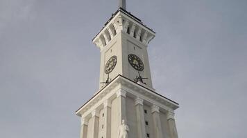 parte inferiore Visualizza di un' orologio Torre con un' lungo guglia su blu nuvoloso cielo sfondo. azione. dettagli di un antico storico costruzione. video
