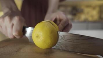 vicino su di signora mani taglio giallo Limone con un' acciaio coltello su un' di legno tavola a il cucina a casa. azione. processi di limonata preparazione. video