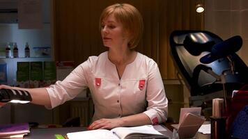 Female scientist sitting at the table in a research center. Stock footage. Concept of pharmacology, woman in a lab with equipment and an opened drug register notebook. video