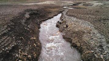 paisaje de seco tierra suelo y río con agua transmisión. disparo. aéreo ver de un campo con grietas y un estrecho río, concepto de ecología y global calentamiento video