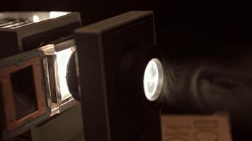 Close up of turning on retro slide projector in a dark room. Stock footage. Old fashioned vintage filmscope turned on n black background. video