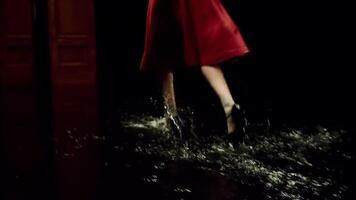 Woman in red dress and summer shoes walking on puddled floor of a dark stage. Stock footage. Dramatic theatre scene with water on the floor and walking actress during performance. video