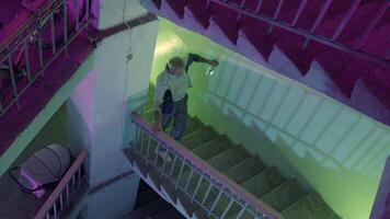 borracho hombre con un vaso botella de vodka molesto a escalada el escaleras. valores imágenes. mayor masculino fanático a alcohol caminando arriba el escalera a obtener hogar rodeado por parpadeo rosado y verde luces video