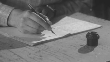Man siting at a desk and using retro fountain pen and inks to make notes. Stock footage. Close up of male hand dipping his pen into inks and starting to write something in a paper notebook, vintage video
