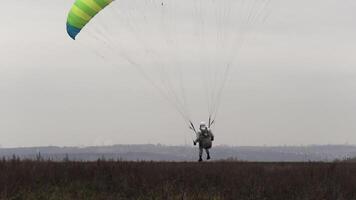 paraglider landning på en vissnade höst fält på molnig himmel bakgrund. handling. fallskärmshoppare slutar hans flyg framgångsrikt. video