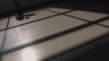 Shadow of a man taking his bag and walking on ceramic tiles floor, leaving a room. Stock footage. Beige clean floor with black window shadows on a sunny day. video