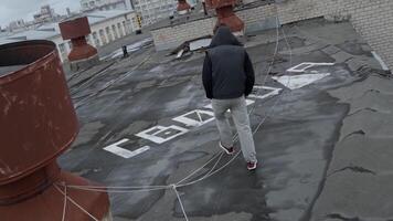 bak- se av en ung tonåring gående på en tak av en bostads- byggnad. stock antal fot. graffiti på tak yta, ord frihet i ryska. video