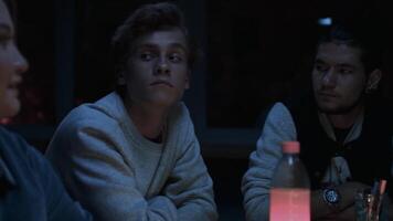 giovane annoiato adolescenti sedersi insieme a il tavolo nel un' buio camera. azione filmato. giovane uomini e donne dentro un' camera senza elettricità. video