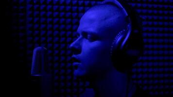 homme en chantant dans enregistrement studio avec microphone. hdr. côté vue de une Jeune Masculin chanteur enregistrement une chanson dans une la musique foncé studio avec bleu lumière. video