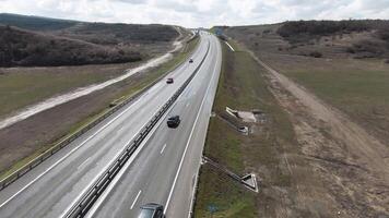 snelweg buiten de stad, panoramisch visie van bovenstaand met het rijden auto's. schot. Rechtdoor snelweg uitrekken langs velden en bossen Aan bewolkt lucht achtergrond. video