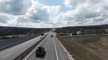 Autoroute à l'extérieur le ville, panoramique vue de au dessus avec conduite voitures. tir. tout droit Autoroute élongation le long de des champs et les forêts sur nuageux ciel Contexte. video