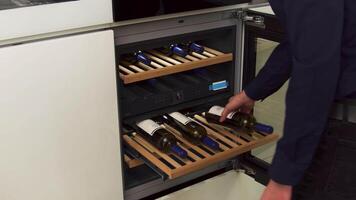 homem levando uma garrafa do vinho a partir de a vinho gabinete às a cozinha às lar. família utensílios. interior detalhes do uma moderno cozinha. video