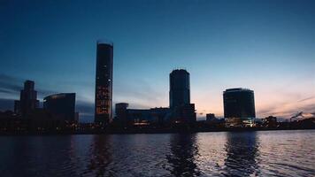 skön landskap med en strömmande flod och blå himmel få mörkare på de solnedgång med en stad på de bakgrund. . Timelapse effekt av en stad med skyskrapor belägen längs de flod. video