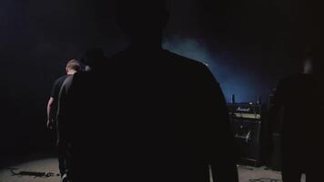 traseiro Visão do masculino Rocha ou metal banda caminhando em Sombrio etapa com instrumentos e fumaça. . conceito do música arte, preparativos para a show. video