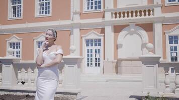 Elegant bride at palace. Action. Gorgeous woman in white dress on background of old building. Woman in stylish white dress poses at palace video