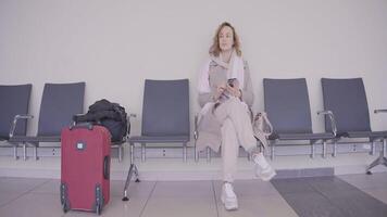 Woman with phone is waiting at train station. Action. Beautiful woman is waiting for flight in waiting room. Woman with suitcase looks at phone at train station video