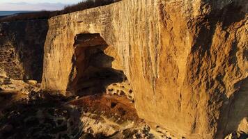 aéreo ver de un gigante acantilado a puesta de sol en un verano soleado día. disparo. masivo pero no profundo arqueado cueva dentro rock formación, hermosa naturaleza. video