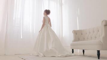 indietro di sposa nel bianca eleganza nozze vestito con ciclo continuo. . pieno lunghezza. nozze. bellissimo sposa in casa con mazzo di fiori contro grande finestra nel pieno lunghezza indietro lato Visualizza video