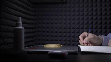 Man writes in notebook on background of black wall. HDR. Young man writes music in notebook. Man writes music or sheet music in notebook in recording studio video