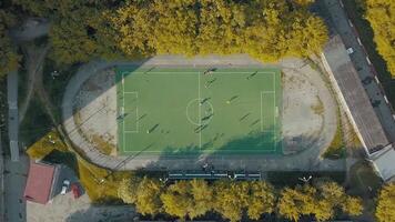 aérien Haut vue de Football équipe pratiquant sur une vert football champ. . en volant au dessus un vieux des sports stade dans une en train de dormir zone de le ville entouré par des arbres et Maisons. video