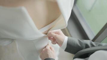 Husband buttoning dress on bride. Action. Close-up of husband helping to fasten bride's dress. Husband romantically fastens dress on wife video