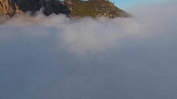 Flying over thick clouds to mountains. Shot. Top view of thick clouds near steep rocky mountains. Beautiful clouds near mountains at dawn video