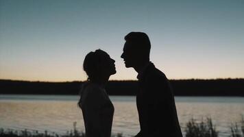 silhouette di un' coppia nel amore a tramonto nel davanti di un' fiume. . lato Visualizza di un' uomo e un' donna baci durante romantico Data, concetto di amore. video