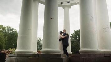 Happy newlyweds dancing surrounded by the columns in the city park. . Bride and groom embracing and dancing on a summer day outdoors. video