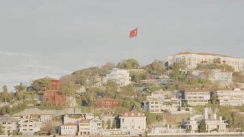 Coast with houses and Turkish flag. Action. Sailing along Turkish coast with flag on hill and residential buildings. Coast of town of Turkey video