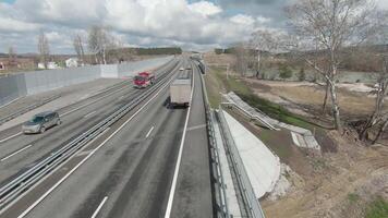 Top view of trucks driving on motorway in spring. Shot. Follow trucks and cars driving along country highway. Drone follows truck on highway on background of cloudy sky video