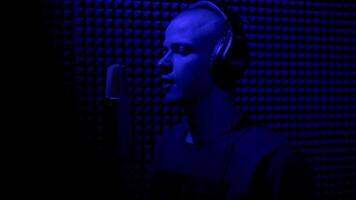 Concept of song writing and creativity. HDR. Close up side view of an enthusiastic young male musician in earphones singing in microphone in sound recording studio booth. video