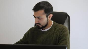 Man is working intently at laptop in office. HDR. Handsome man is working at laptop in sweater. Freelancer or writer working on laptop video