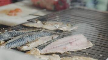 avvicinamento di grigliate pesce. azione. fresco pelato pesce è grigliato su griglia. grigliato pesce nel strada stalla. cucinando delizioso grigliato pesce su griglia video