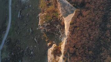 Top view of rocky cliff line. Shot. Rocky cliff is illuminated by sun's rays on background of dark plain at foot. Beautiful rocky cliff in morning or evening sun video