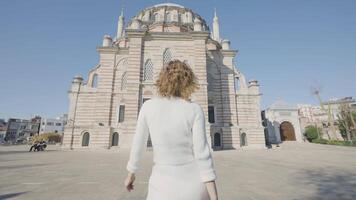 Beautiful woman goes to mosque. Action. Rear view of beautiful woman walking in front of mosque. Attractive woman walks into mosque on sunny day in Istanbul video