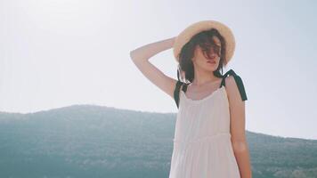 mooi slank vrouw met gekruld haar- in wit jurk en een hoed onder de helder zon. actie. model- poseren in voorkant van een berg Aan Doorzichtig lucht achtergrond. video