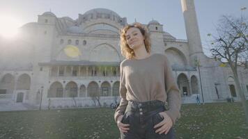 Beautiful woman poses at mosque. Action. Happy woman twirls and poses on background of historic temple. Attractive woman happily poses outside mosque on sunny day video