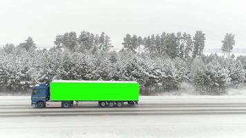 aéreo ver de un la carretera en idílico invierno paisaje y un conducción camión con croma llave verde sitio en el lado de sus cuerpo. escena. concepto de publicidad y transporte. video