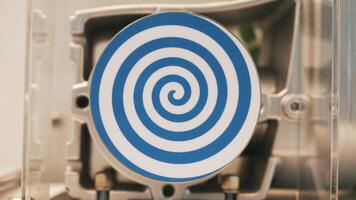 Close up of rotating white flat circle with bright blue spiral that creating hypnotic effect. HDR. Unusual robot with automated spinning hypnotic circle. video