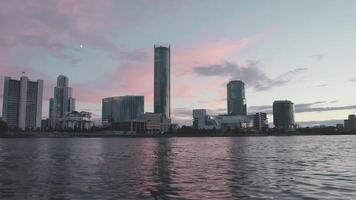 sommar solnedgång landskap med ett jag ställer torn i främre av de krusigt flod Jekaterinburg, Ryssland. . rosa och blå kväll himmel ovan skön arkitektur och en flod. video