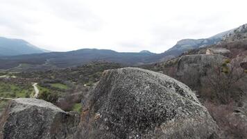 Boulders expanse at the foots of mountain range. Shot. Aerial view of a wild valley covered by stones, greenery and crossed by narrow paths on cloudy sky background. video