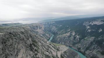 aéreo Visão do montanhoso região com fluindo Largo calma rio. Ação. tirar o fôlego selvagem panorama com Alto penhascos, rio, e nublado céu em uma verão dia. video