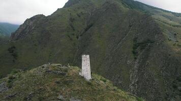 aéreo Visão do a antigo velório construção tsoy pede, a checheno república, Rússia. Ação. branco torre em a topo do uma verde Colina cercado de montanhas. video