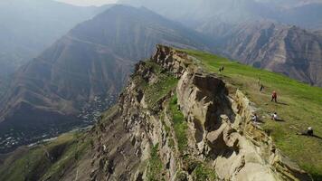 Top view of travelers on rocky cliff on background of high mountains. Action. Breathtaking view from cliff to mountain valley with air veil. High green mountains with light fog on sunny day video